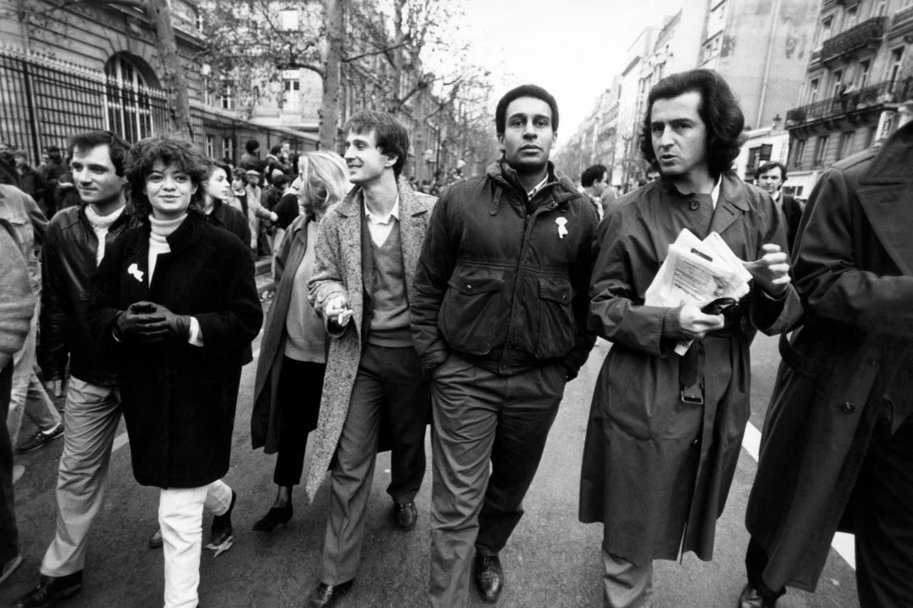 Photo en noir et blanc de Bernard-Henri Lévy aux côtés de Harlem Désir lors de la manifestation organisée à Paris en mémoire de Malik Oussekine, le 6 décembre 1986.