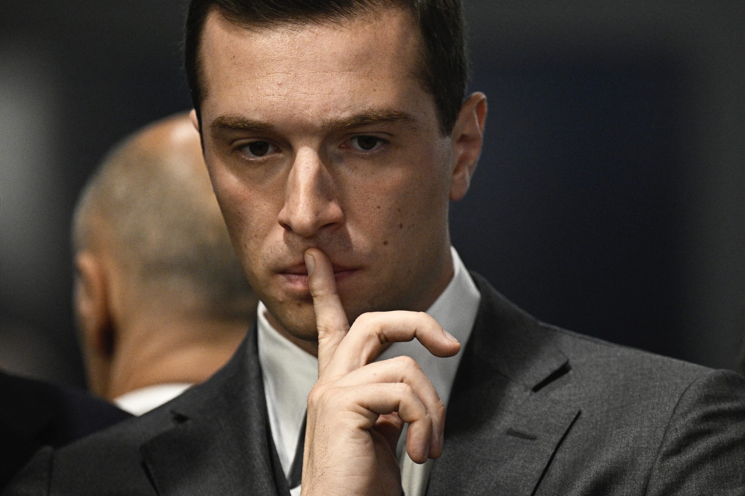 Portrait de Jordan Bardella , il met un doigt sur sa bouche.